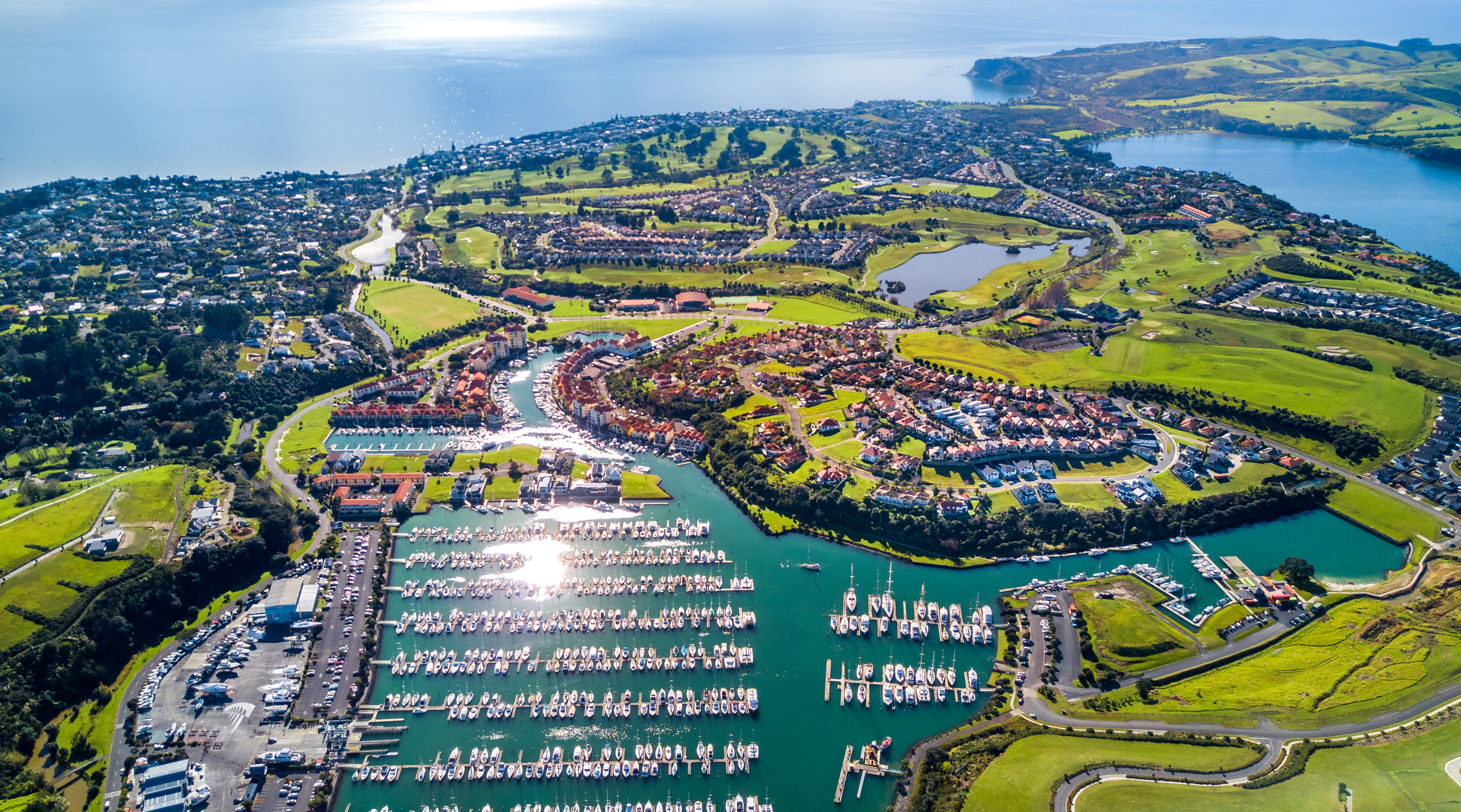 Aerial view of residential suburbs on Whangaparaoa Peninsula, Auckland, New Zealand, bordered by a sunny ocean harbour