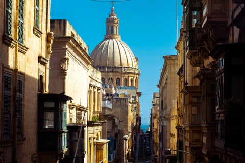 Street view in the city center of Sliema, Malta, featuring typical Maltese houses with balconies and the Stella Maris Parish Church visible in the background