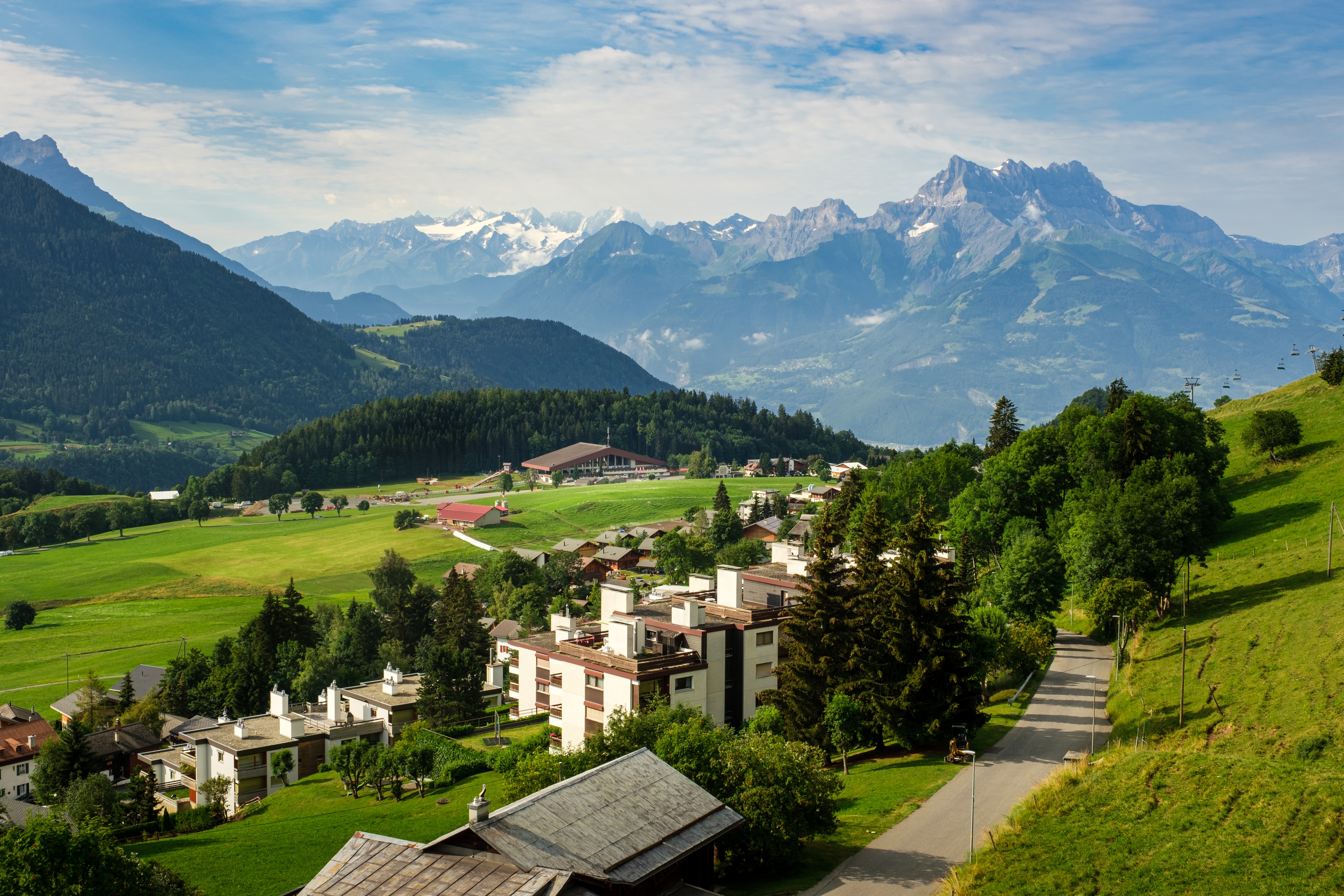 View of Leysin, Switzerland, showing alpine houses nestled among green meadows with mountains in the background