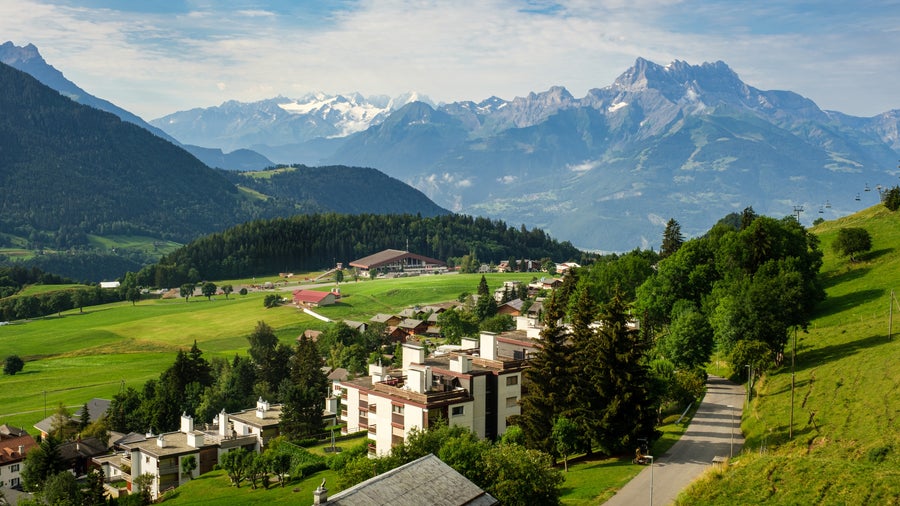 View of Leysin, Switzerland, showing alpine houses nestled among green meadows with mountains in the background