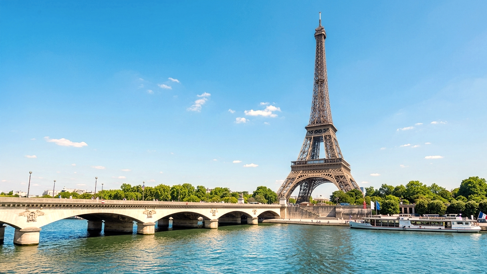 A wide-angle view of the Eiffel Tower rising above the Seine River and the Pont d'Iéna bridge in Paris, France, on a sunny day, representing the iconic cultural backdrop for language study abroad programs.