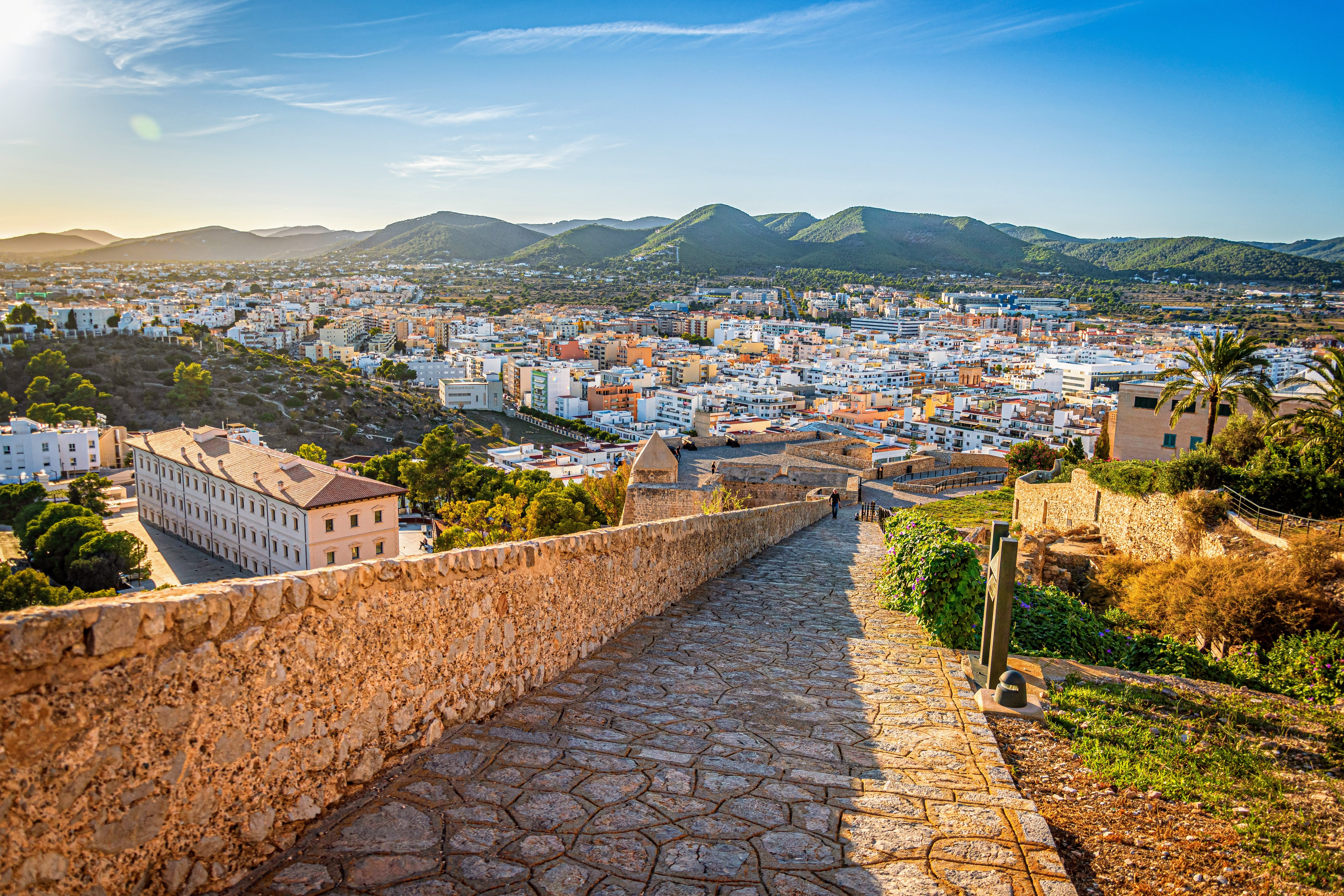 Aerial view of Ibiza, Spain with a rustic path descending towards the town, and mountains in the background