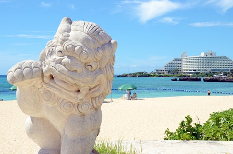 Traditional Ryukyuan Shisa lion statue standing on a pristine white sand beach in Okinawa, Japan