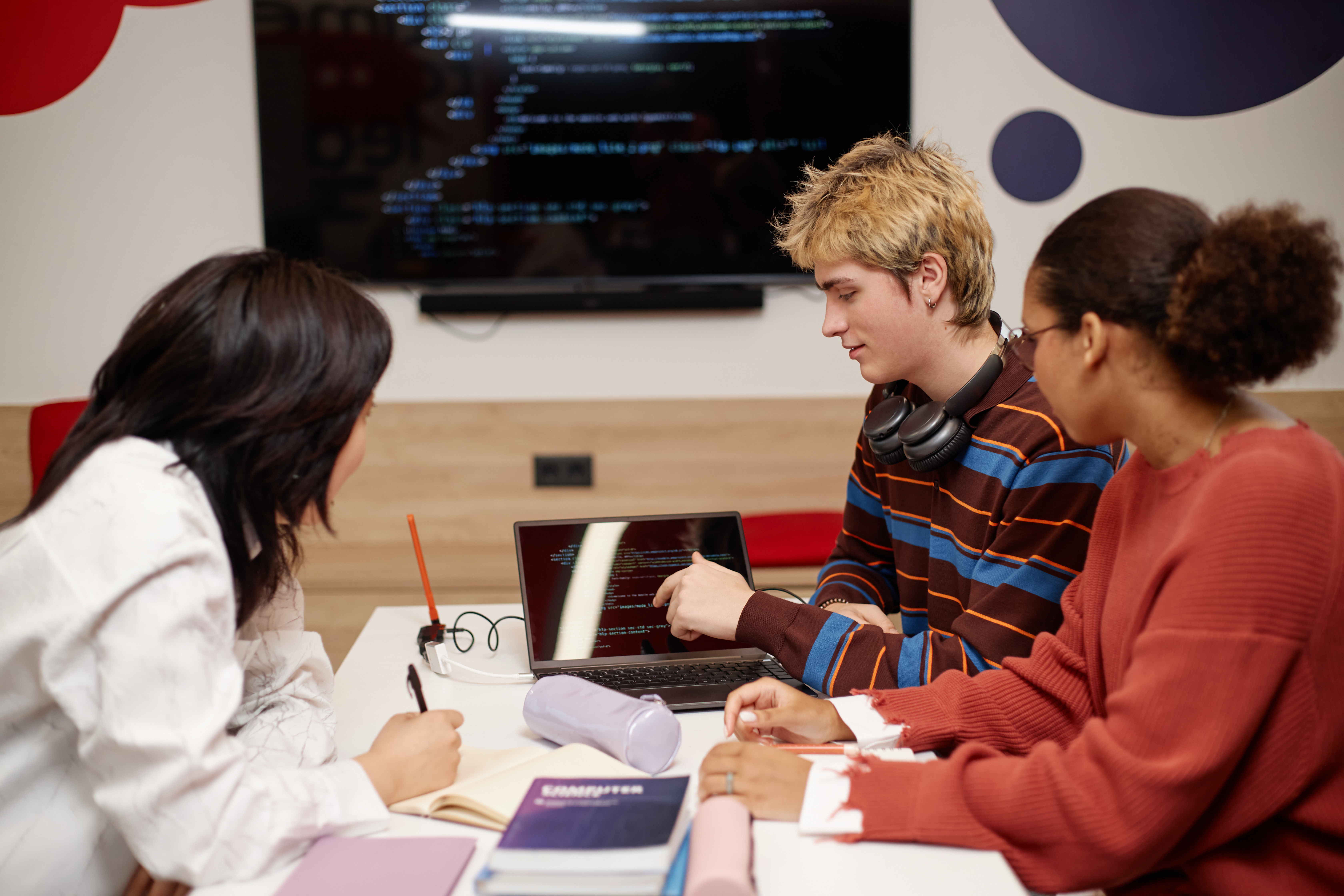 Diverse group of college students studying IT together at table in school library and using laptop with code lines on screen