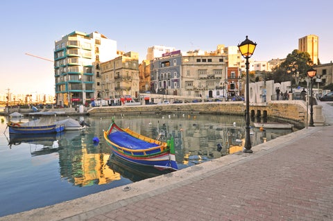 St. Julian's waterfront in Malta with boats anchored in the calm sea and coastal buildings lining the shore