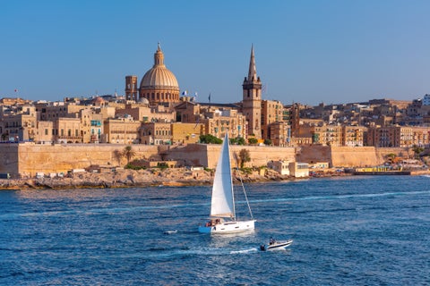 Boats floating in the Mediterranean Sea off the coast of Sliema, Malta, with historic landmarks in the background including Fort Tigné and the Manoel Island Fortress