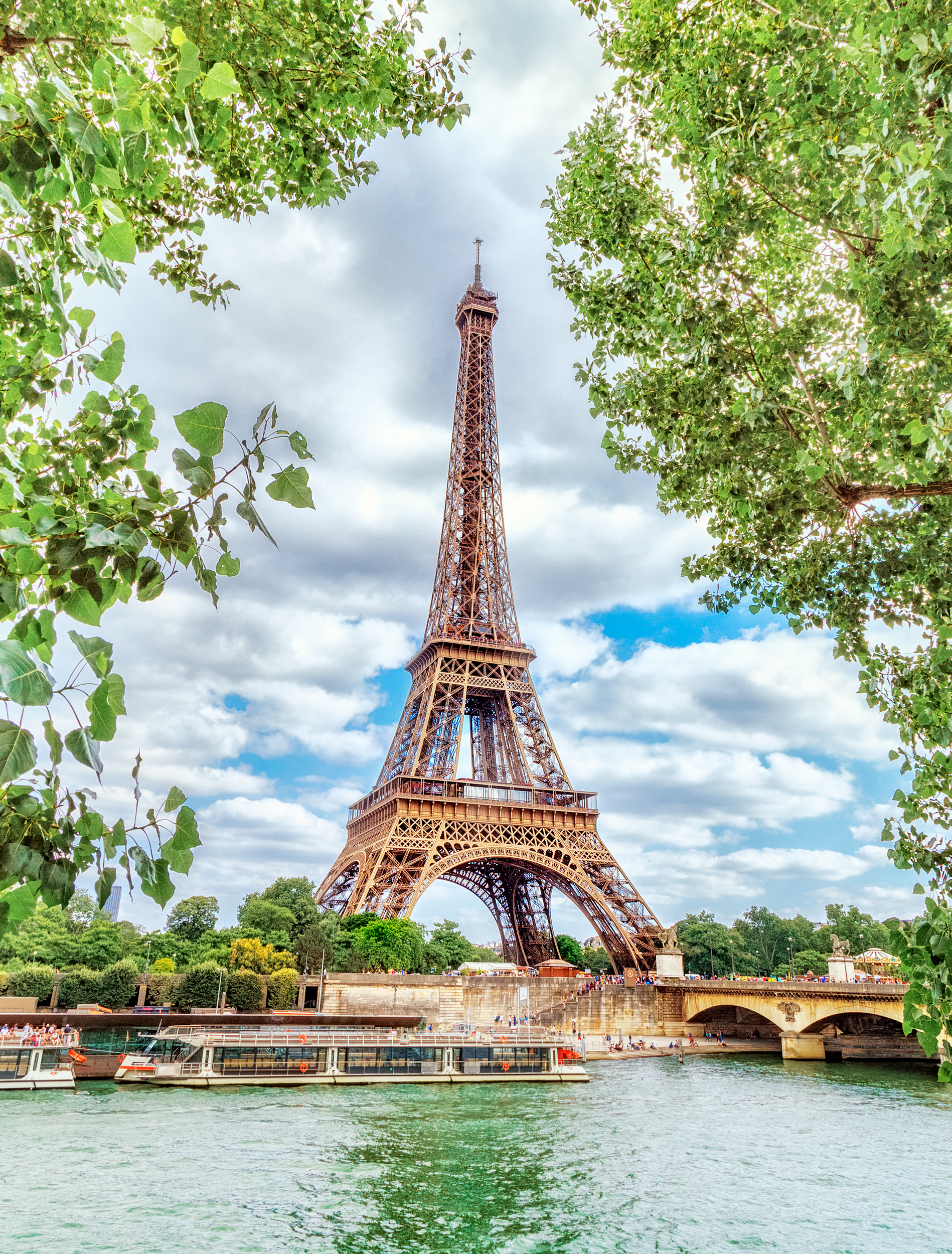 Tourist boat on the Seine River with trees in the foreground and the Eiffel Tower in Paris France on a sunny day