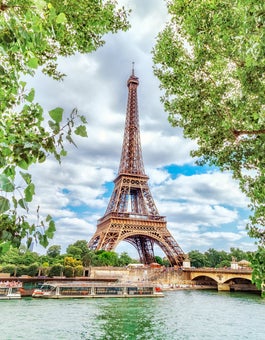 Tourist boat on the Seine River with trees in the foreground and the Eiffel Tower in Paris France on a sunny day