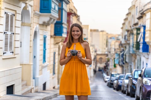 Young girl holding a camera while exploring the vibrant streets of Sliema, Malta, with a backdrop of historic buildings and local charm