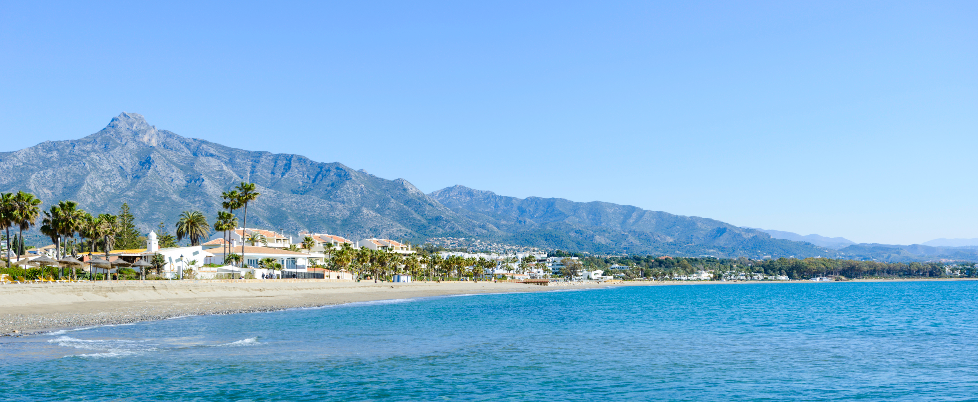 Beach in Marbella, Spain with sun loungers and umbrellas, and the Sierra Blanca mountains in the background