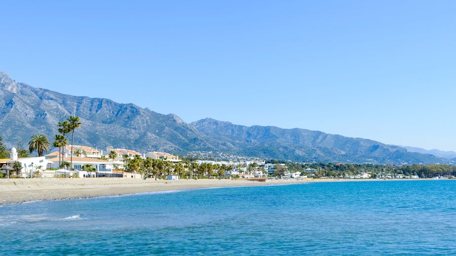 Beach in Marbella, Spain with sun loungers and umbrellas, and the Sierra Blanca mountains in the background