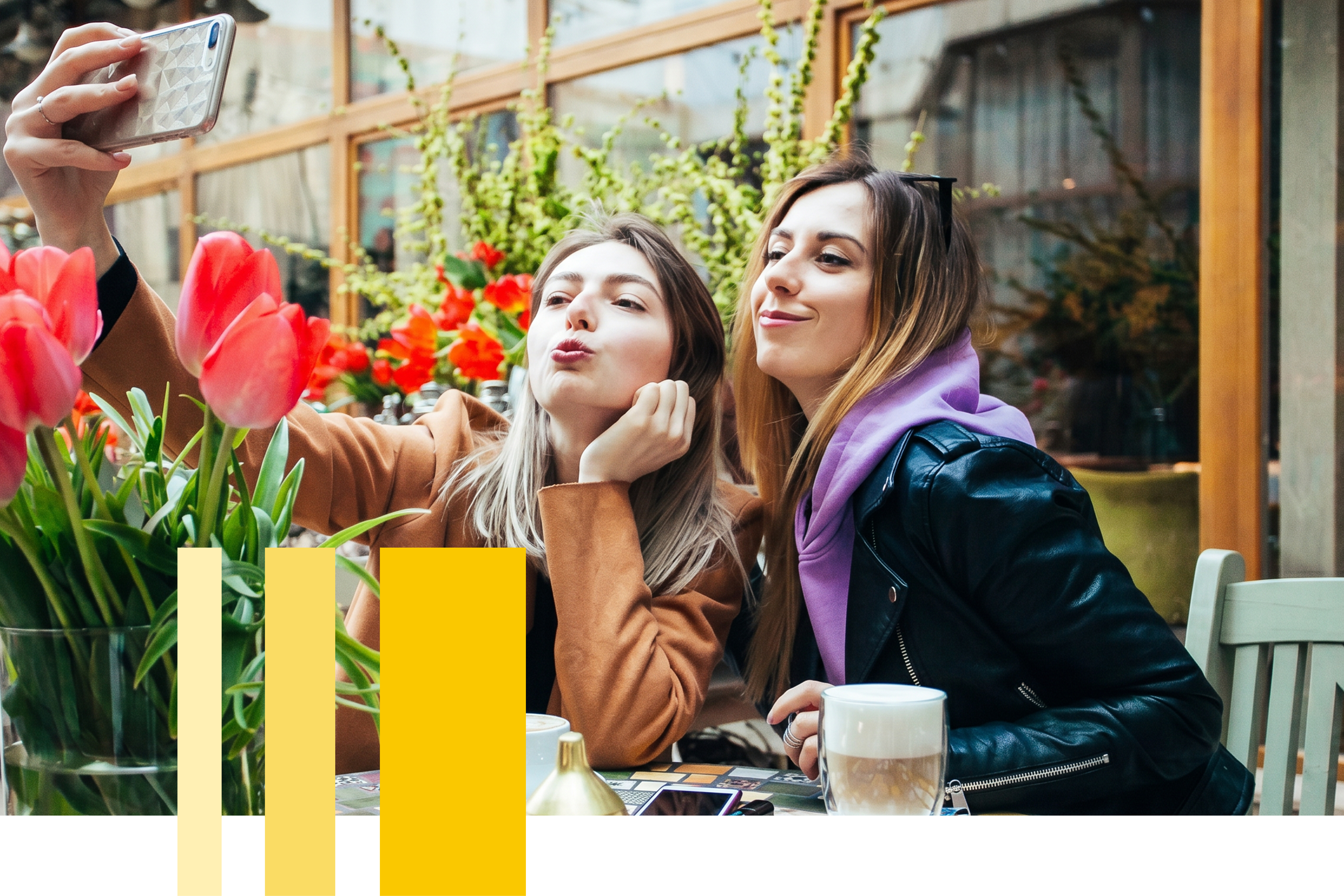 A group of four happy, diverse young women embracing and taking a selfie with a smartphone by the Seine River in Paris, with historic French architecture in the background, representing the friendships formed during a language study abroad program.