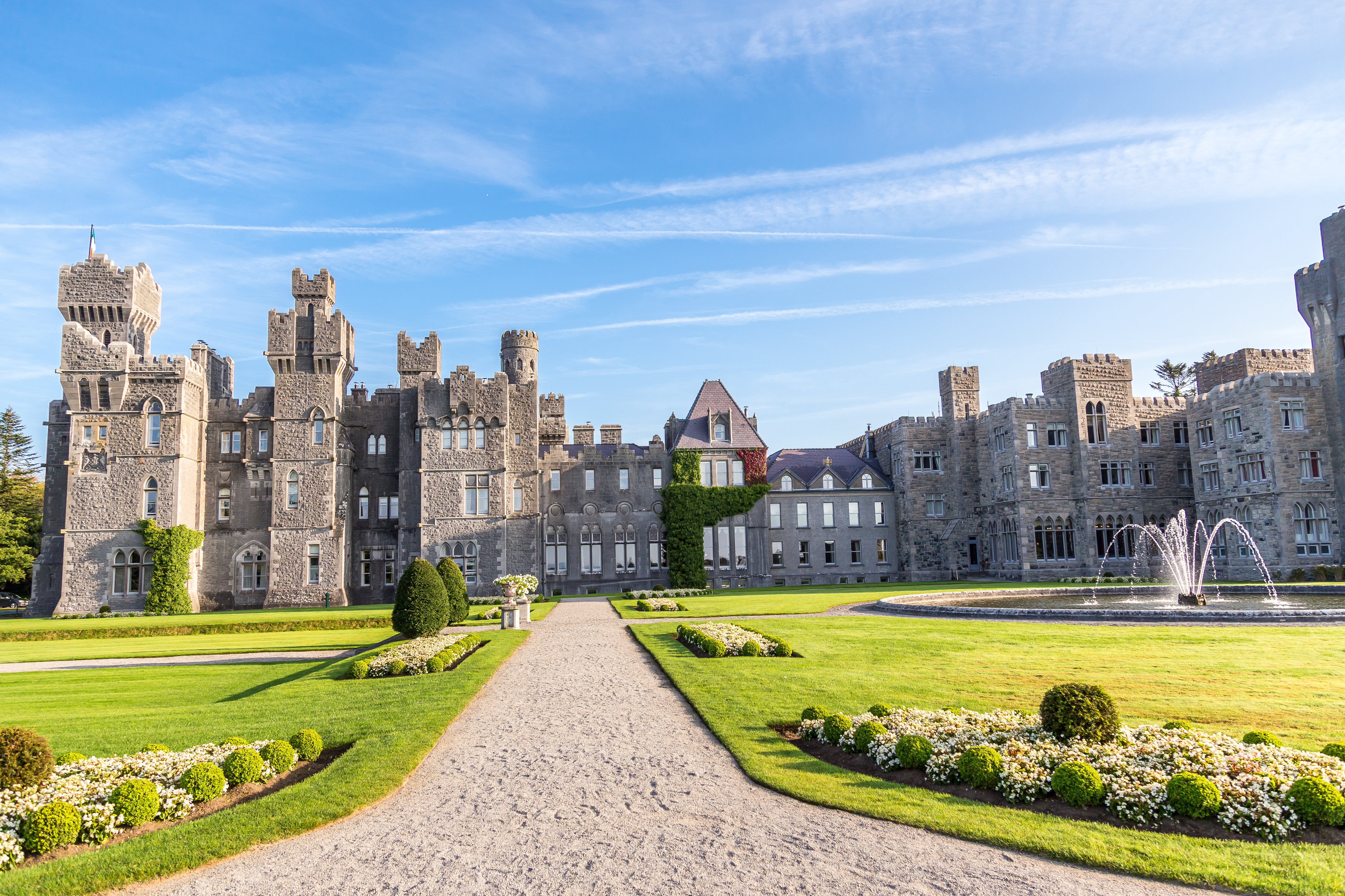 Ashford Castle in County Mayo, Ireland, with its medieval architecture surrounded by sprawling manicured gardens and lush woodlands.