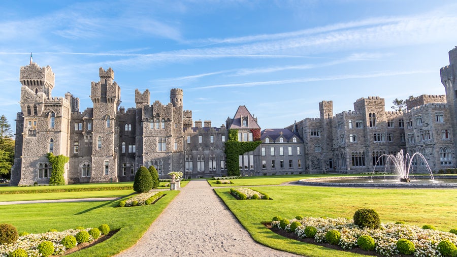Ashford Castle in County Mayo, Ireland, with its medieval architecture surrounded by sprawling manicured gardens and lush woodlands.