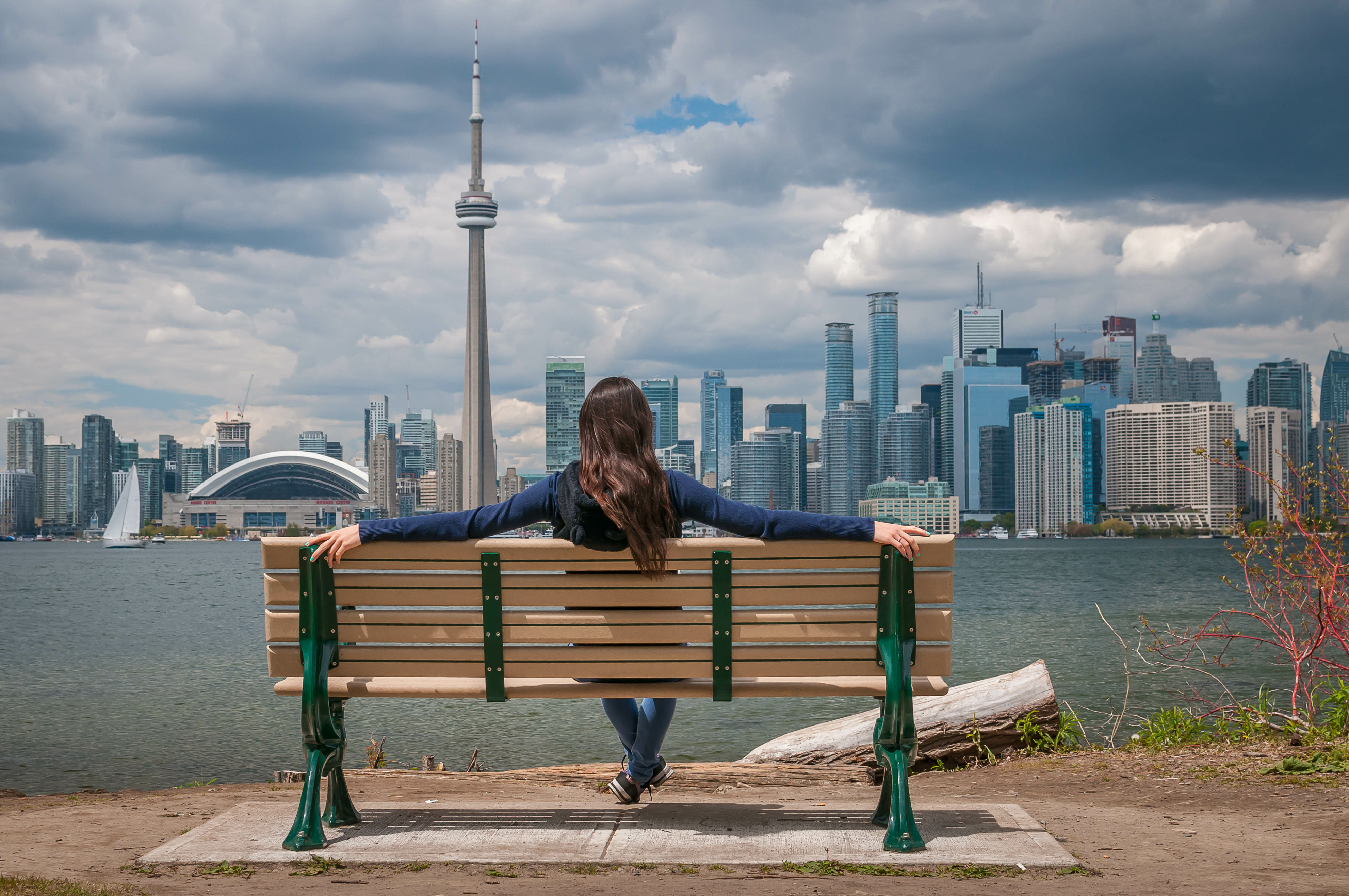 Girl seated on a bench viewing Toronto skyline across Lake Ontario, Canada