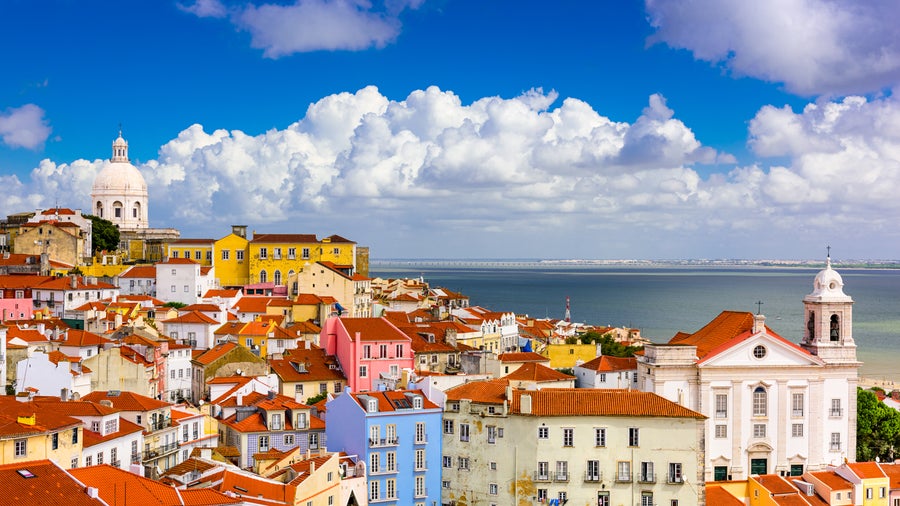 Aerial view of Alfama district in Lisbon with terracotta roofs, Lisbon Cathedral, São Jorge Castle, and the Tagus River in the background