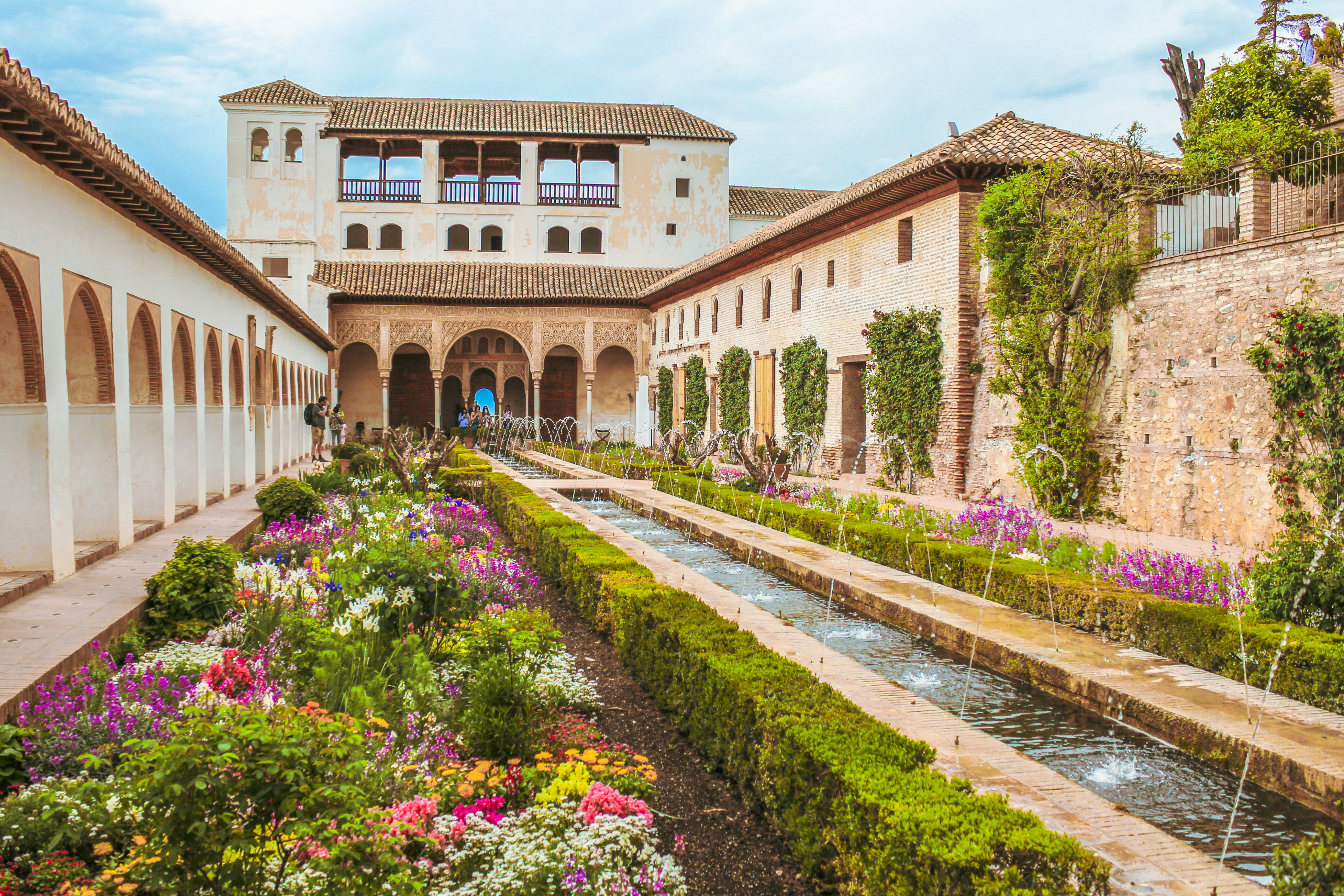 Lush garden with vibrant flowers and Moorish architecture in Granada, Spain, likely part of the Alhambra or Generalife