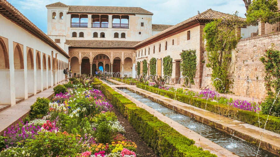 Lush garden with vibrant flowers and Moorish architecture in Granada, Spain, likely part of the Alhambra or Generalife