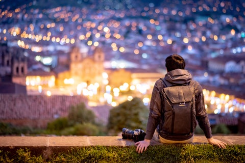 Tourist sitting atop a hill overlooking the night lights of Cusco city center, Peru