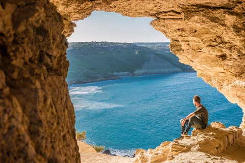Man enjoying sea view through a natural rock window on a hill in Gozo, Malta