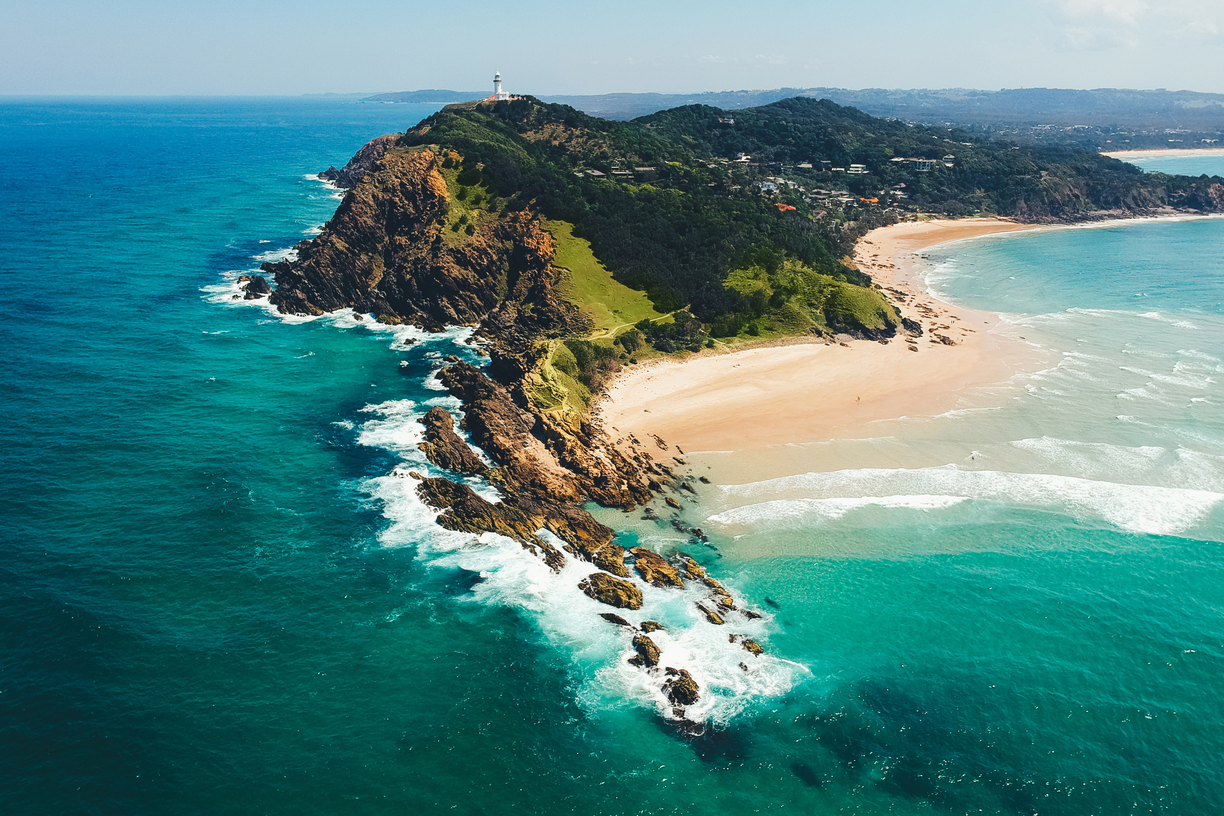 Aerial view of Byron Bay surrounded by lush greenery and overlooking the turquoise waters of the Pacific Ocean