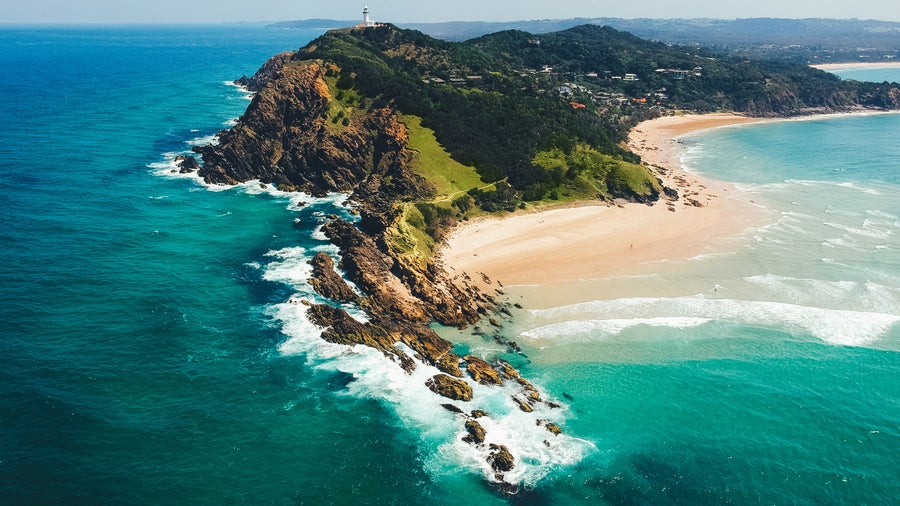 Aerial view of Byron Bay surrounded by lush greenery and overlooking the turquoise waters of the Pacific Ocean