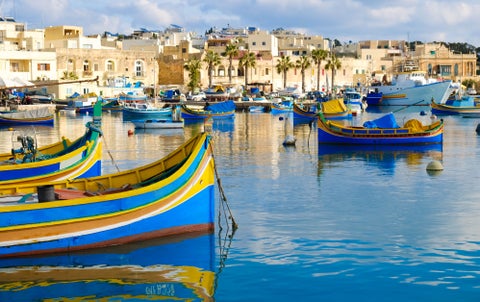 Colourful fishing boats moored in the Grand Harbour of Valletta, Malta, with the city’s historic limestone buildings rising in the background