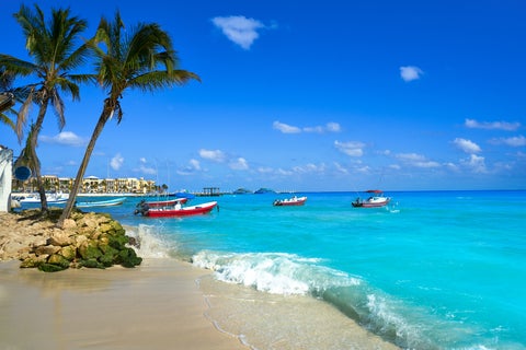Playa del Carmen beach in Mexico with boats on the turquoise sea and palm trees lining the sandy shore