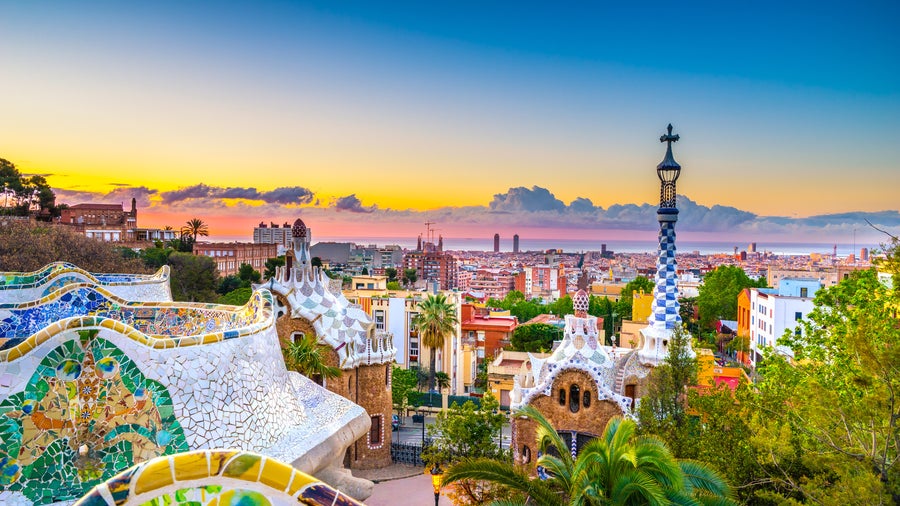 View of Park Güell in Barcelona, Spain, featuring colorful mosaic tiles, whimsical architectural elements, and lush greenery against the city backdrop