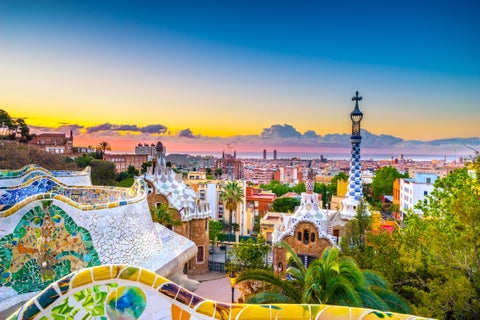 View of Park Güell in Barcelona, Spain, featuring colorful mosaic tiles, whimsical architectural elements, and lush greenery against the city backdrop