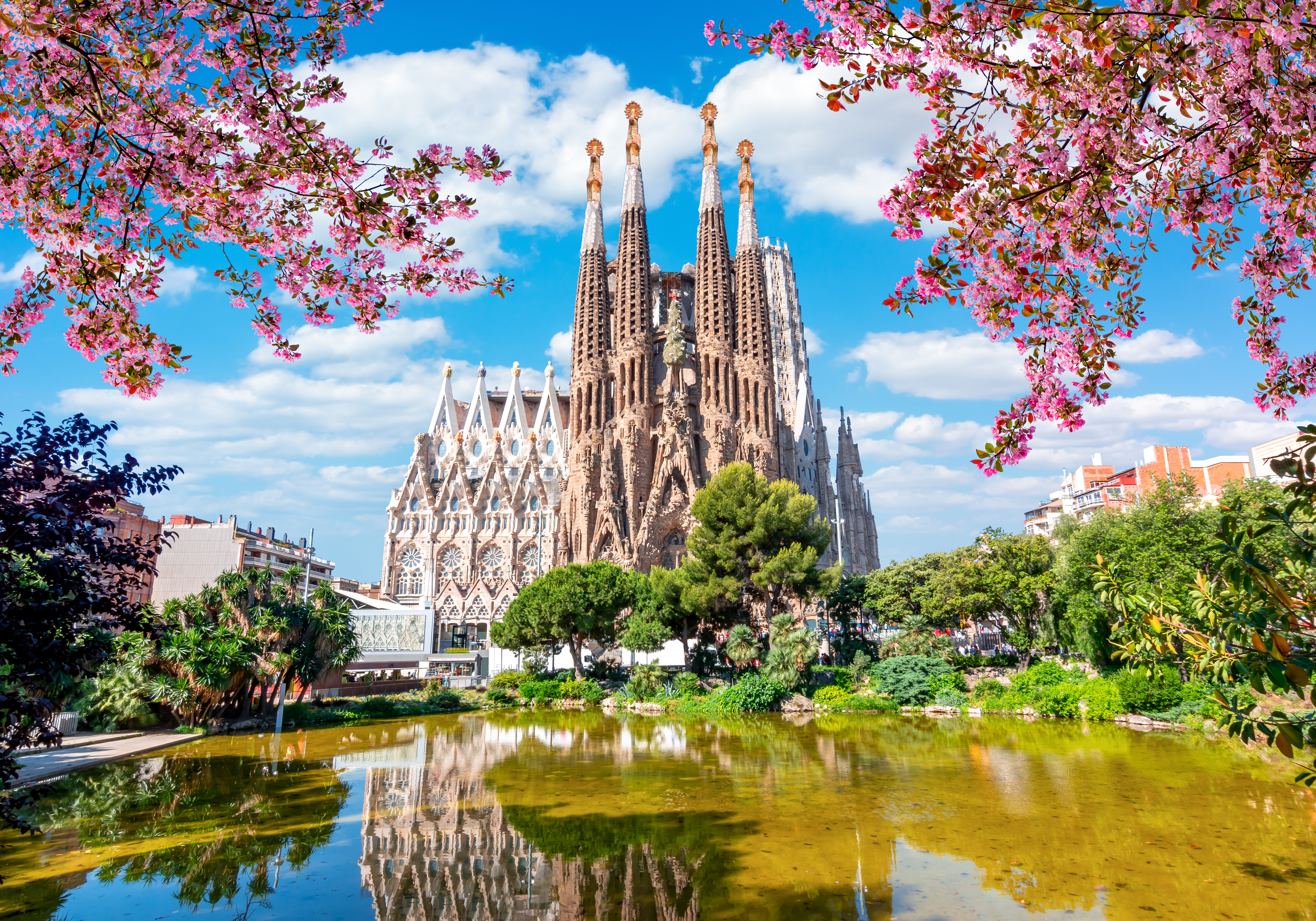 Sagrada Familia Cathedral in Barcelona, Spain, surrounded by springtime greenery and blooming flowers under a clear sky