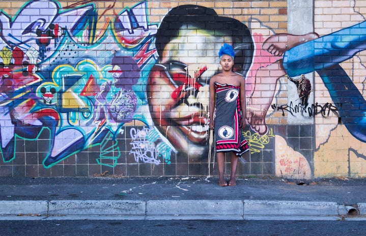 African girl wearing tradition clothing in front of a wall filled with graffiti, a common way Africans express their creativity.