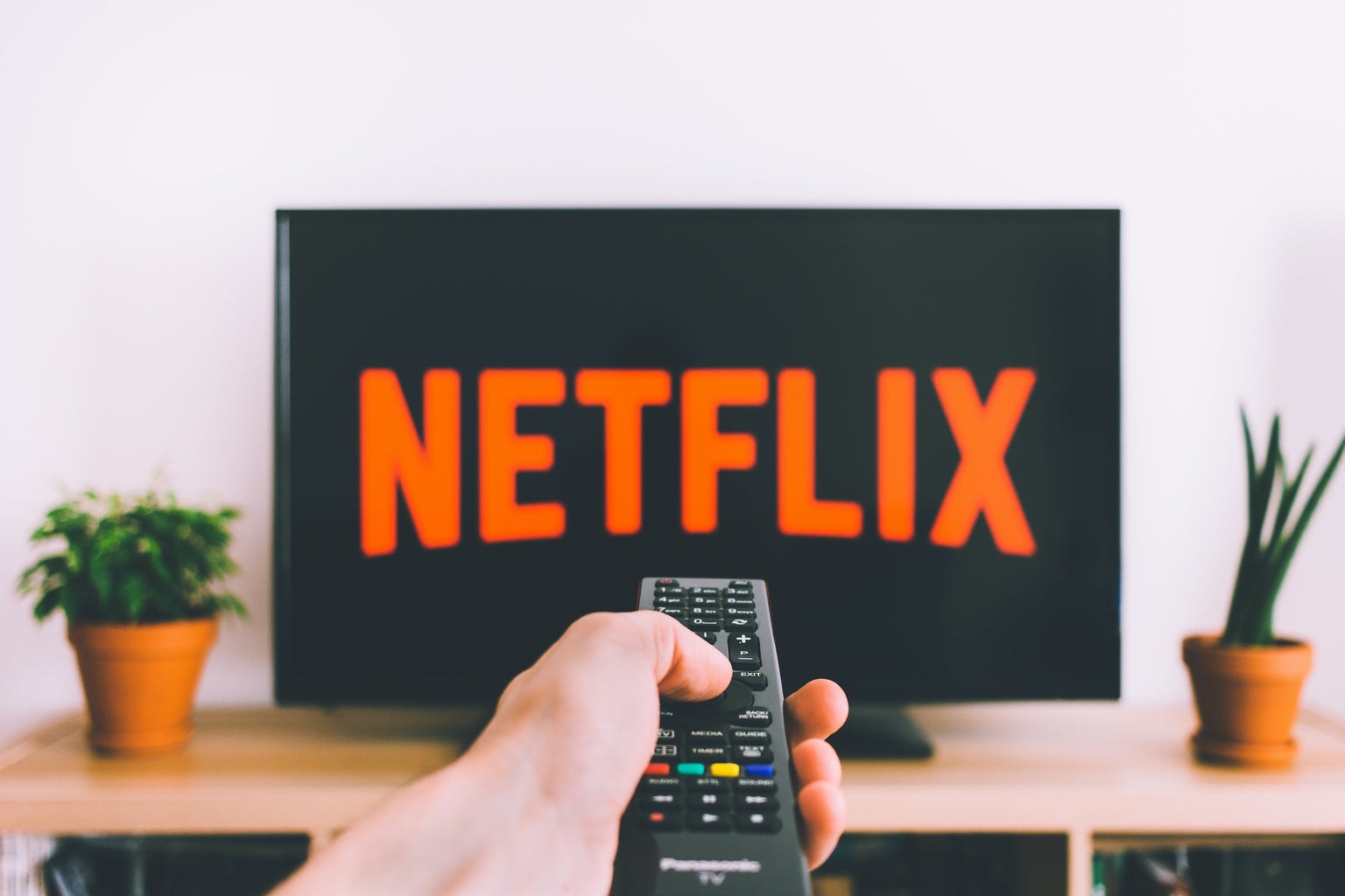 person holding a remote control pointed at TV streaming netflix