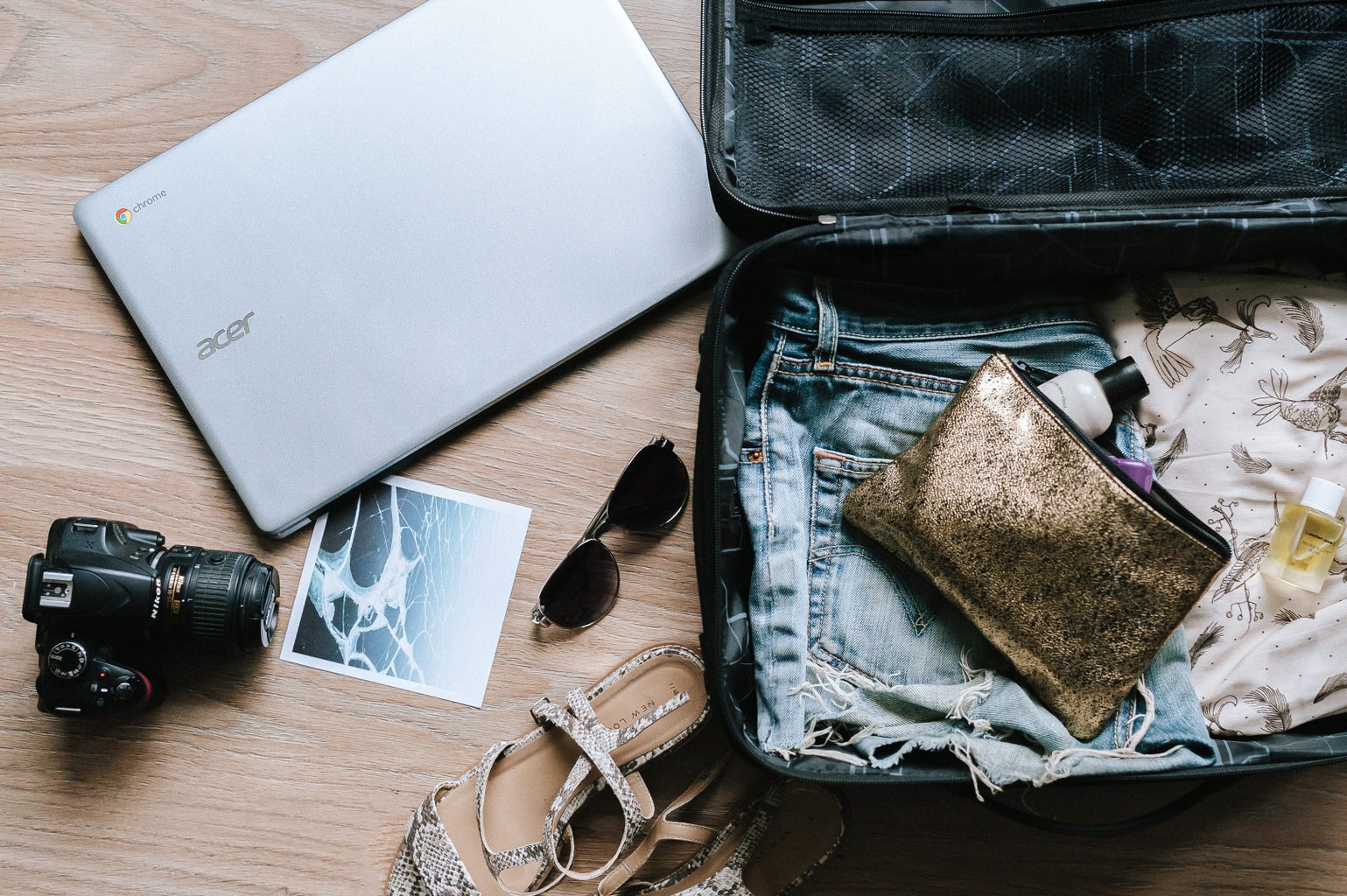 open suitcase with a laptop, camera, a photo, and sunglasses lying around it
