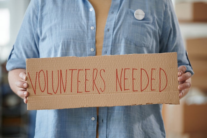 A Person Holding a Cardboard with Inscription \'Volunteers Needed\'