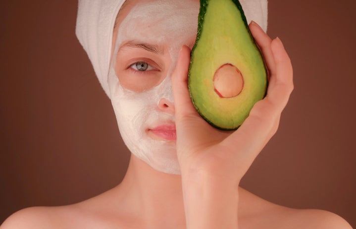 woman with white face mask holding an avocado