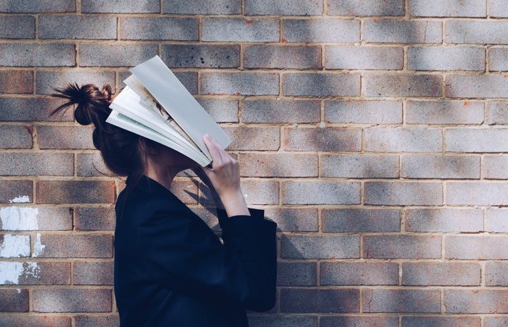 girl standing in front of brick wall holding book up to her face