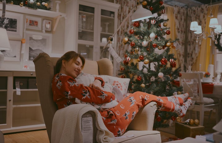 woman in pajamas hugging a pillow with christmas tree in background