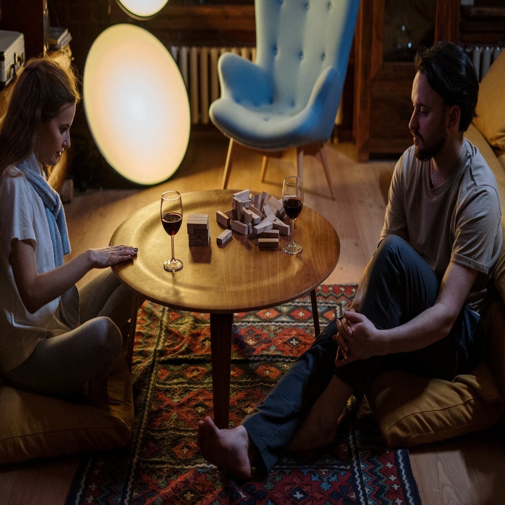 man and woman playing jenga on wooden floor table with wine