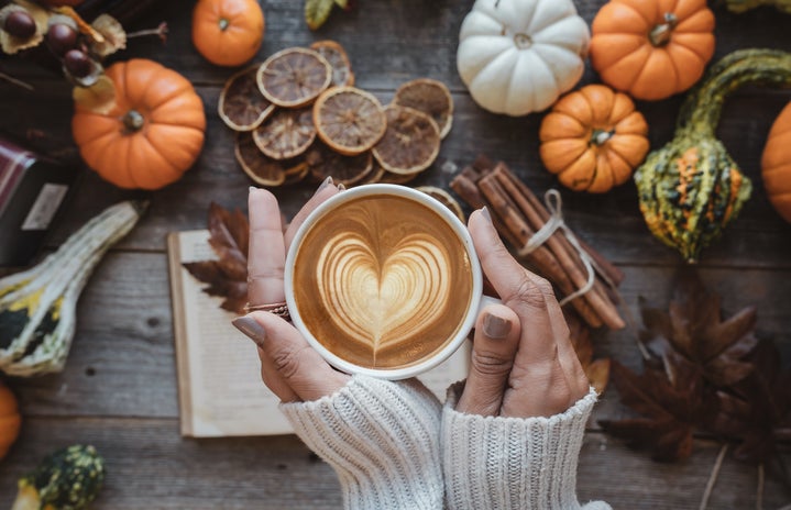 Hands holding latte with fall themed items
