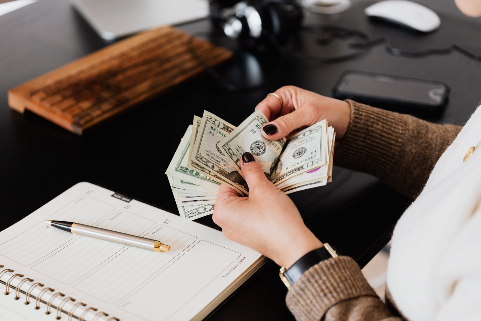 woman counting money near notebook on desk