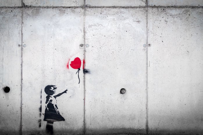 Spray painted on a grey wall - a little girl wearing a dress reaches for a red balloon.
