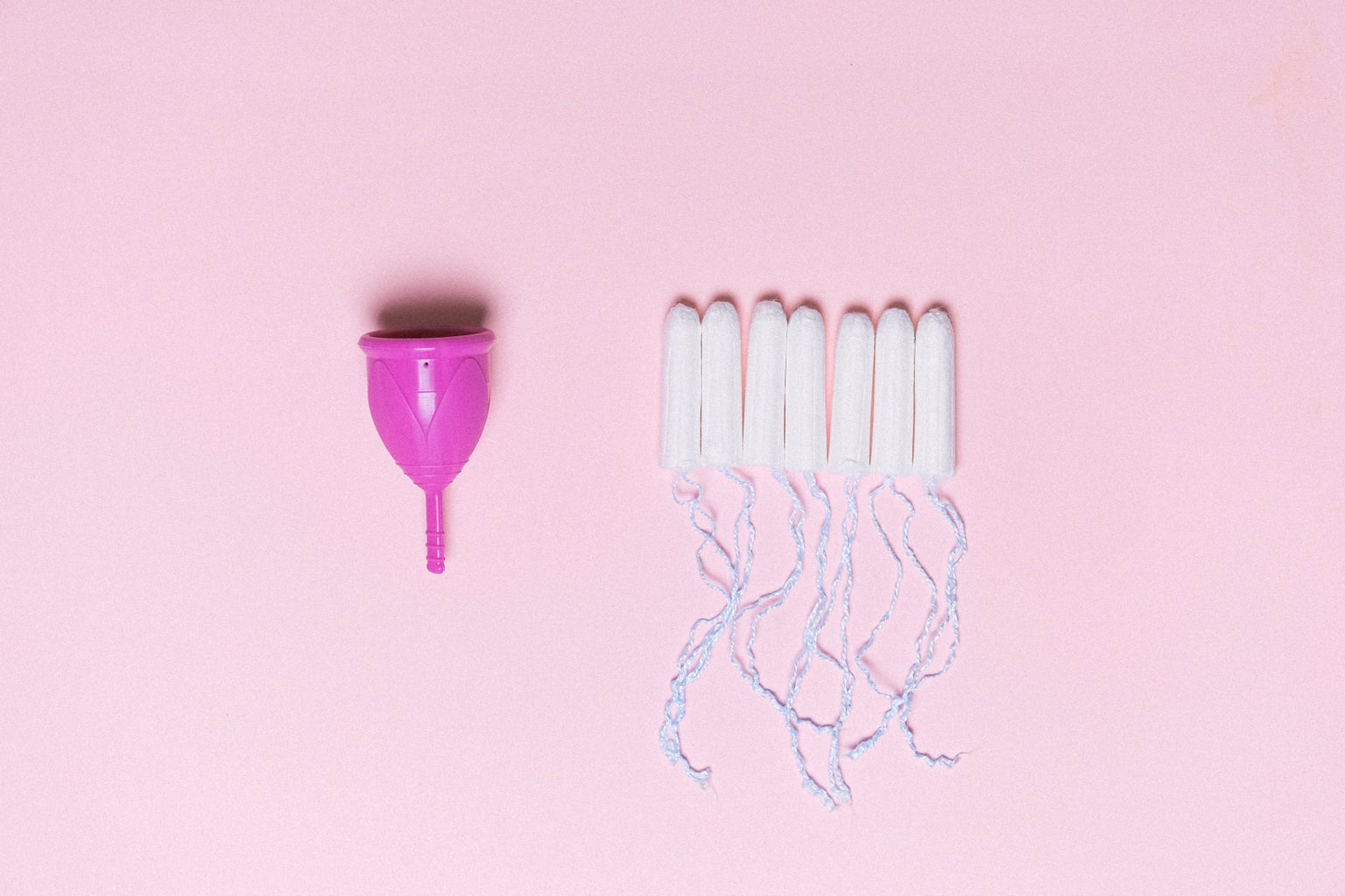 Menstrual Cup next to tampons on a pink background
