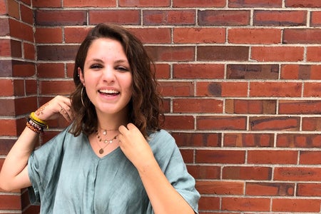 a girl standing and smiling in front of a brick wall