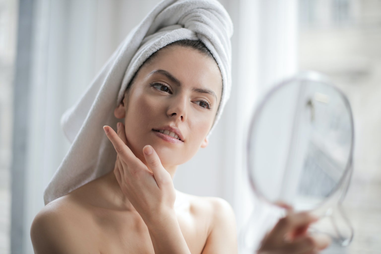 woman with towel on her head looking at herself in the mirror, clear skin