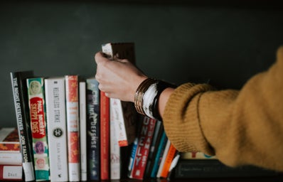 A hand picking up a book from a shelf.