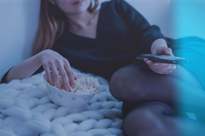 woman laying on side with remote eating popcorn