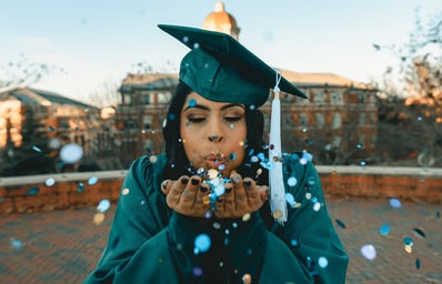 woman in green graduation gown blowing confetti