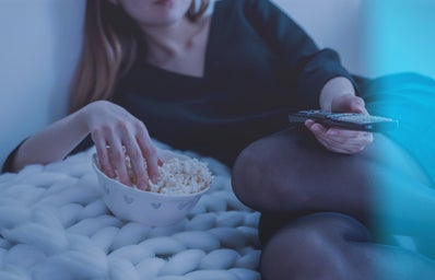 Woman in White Bed Holding Remote Control While Eating Popcorn
