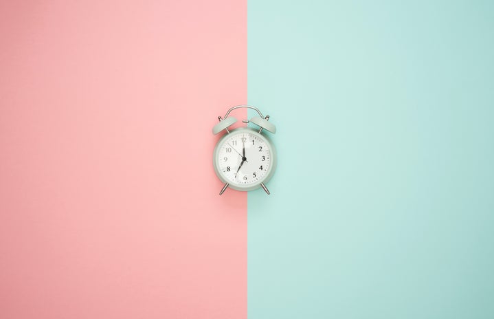 blue clock on a pastel background that is half pink and half blue